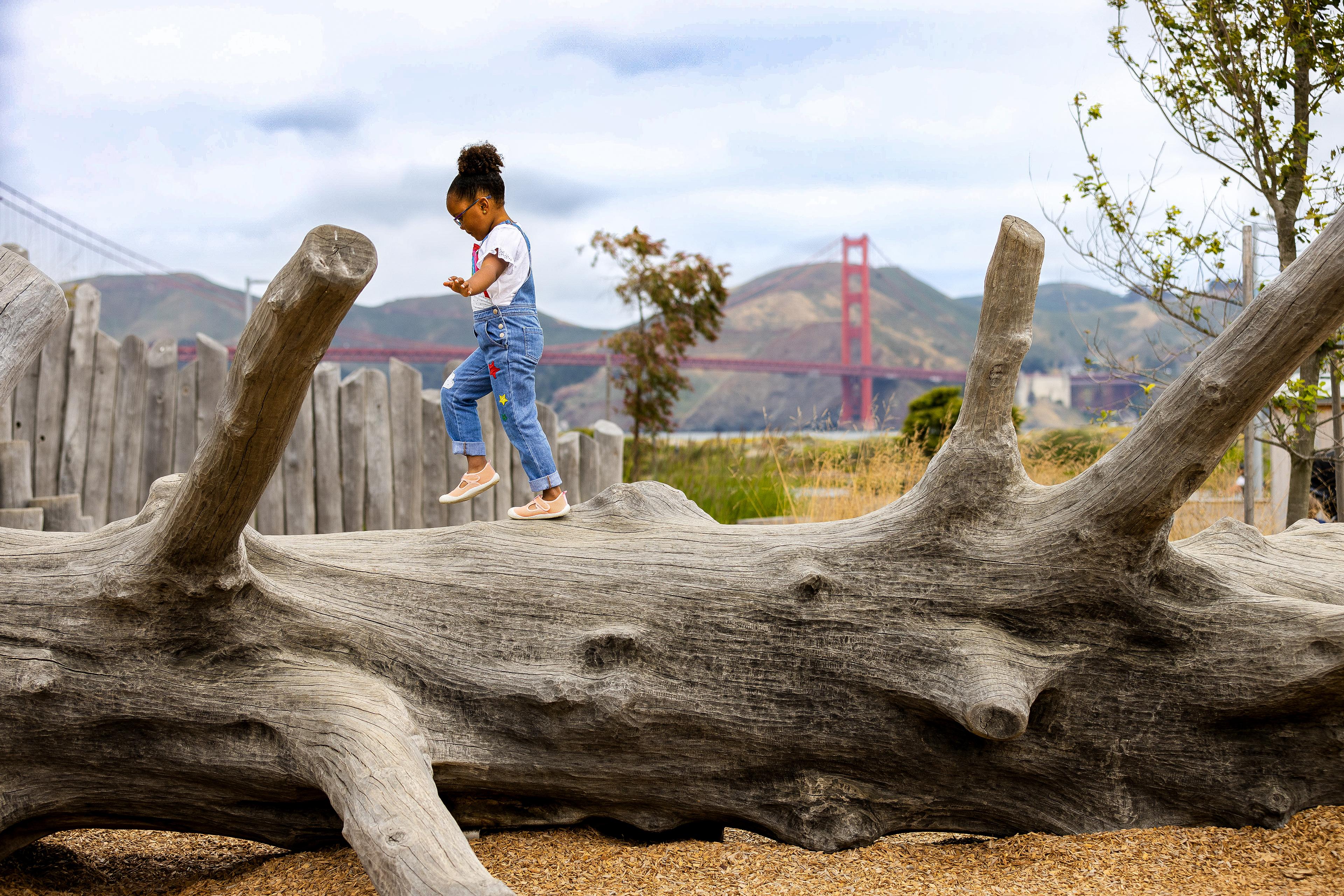 Little girl walking across a log in the Outpost Playgorund with the Golden Gate Bridge in the background