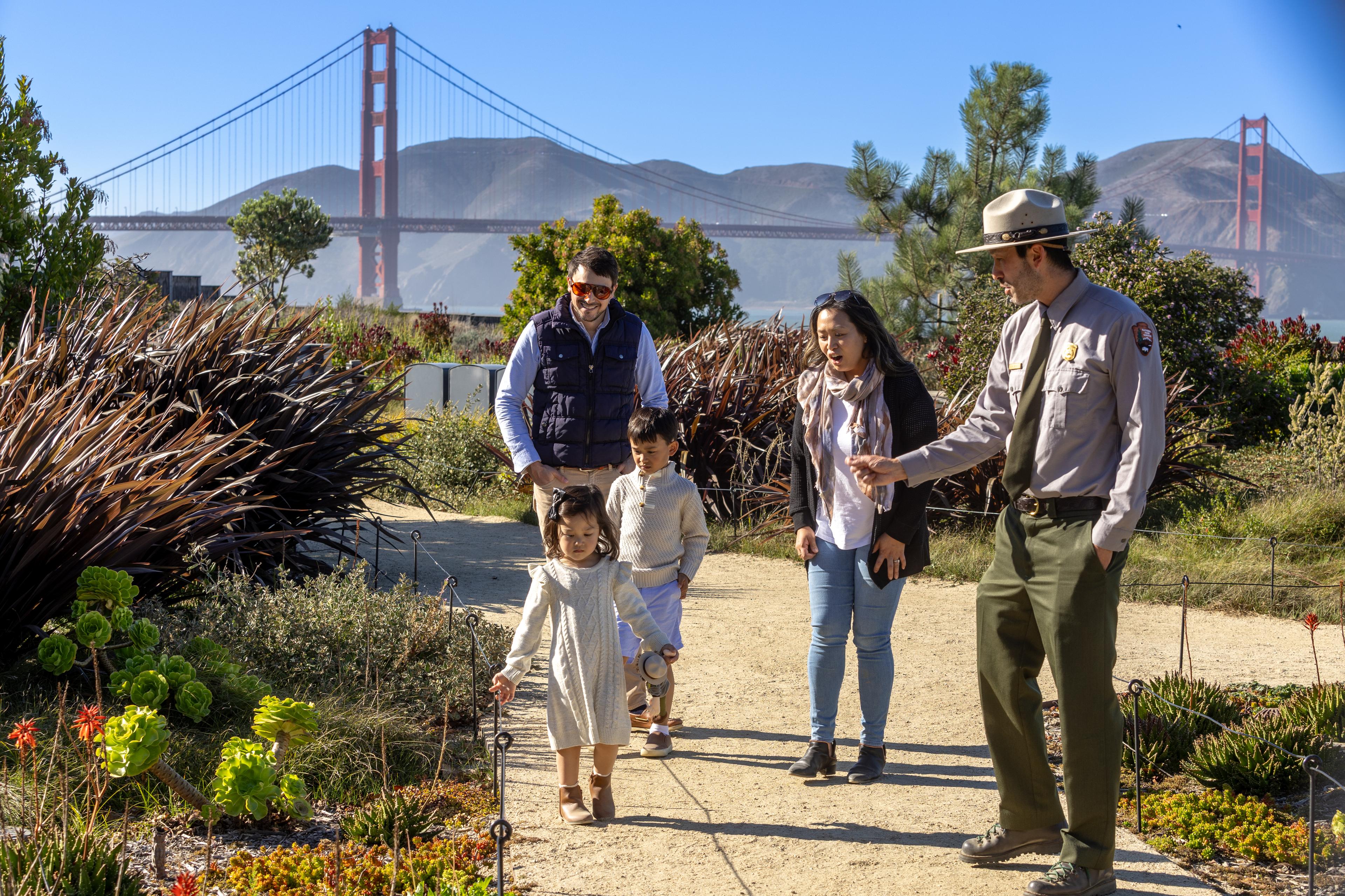 family of four with young children running along the Presidio Tunnel Tops with a National Parks Ranger with the Golden Gate Bridge in the background,